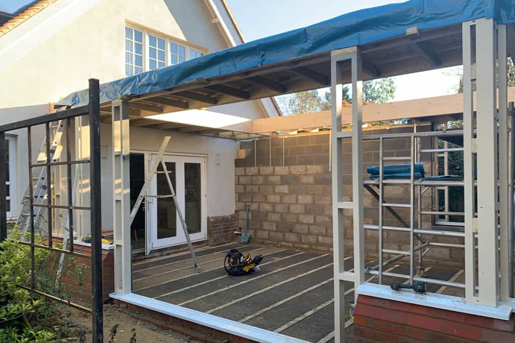 Timber posts and roof beams being assembled beneath a temporary weather cover