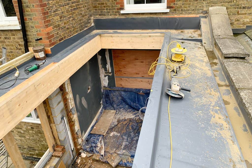 Orangery roof under construction with timber beams and waterproofing beside the party wall