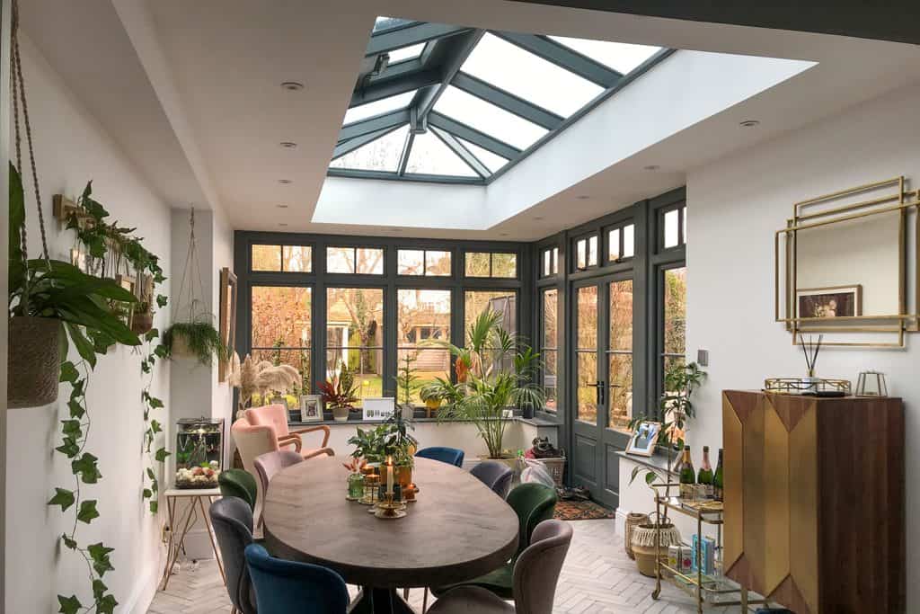 Finished orangery dining room with a round table, dark grey windows and glazed roof lantern