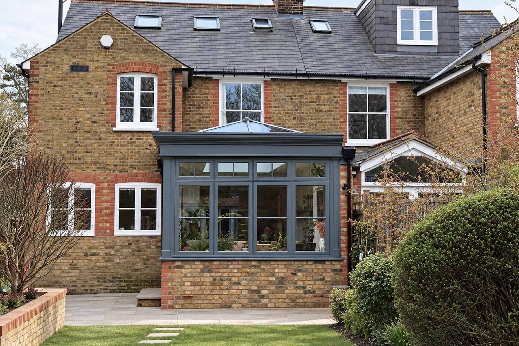Dark grey orangery attached to a Victorian brick house in St Albans, viewed from the garden