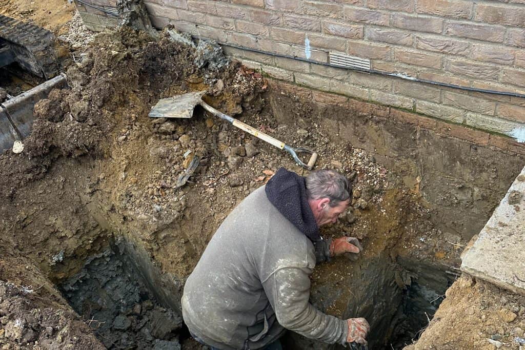 Builder examining a trial hole beside the house before foundation work
